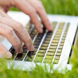 一个人坐在草地上用笔记本电脑打字的特写图像.